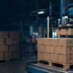 Your Best Packer and Your Worst Packer - Korpack - Packaging Solutions for Complex Businesses Industrial robotic arm lifts a cardboard box onto a pallet in a dimly lit warehouse environment