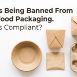 pfas free - Korpack - Packaging Solutions for Complex Businesses Bold headline about PFAS ban on fiber food packaging with scattered kraft paper boxes, cups, and a muffin tray on a white background.