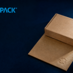 ChatGPT Image Aug 11 2026 01_53_01 PM - Korpack - Packaging Solutions for Complex Businesses KORPACK logo on a dark blue background with brown cardboard boxes and packing material nearby in a studio setup.