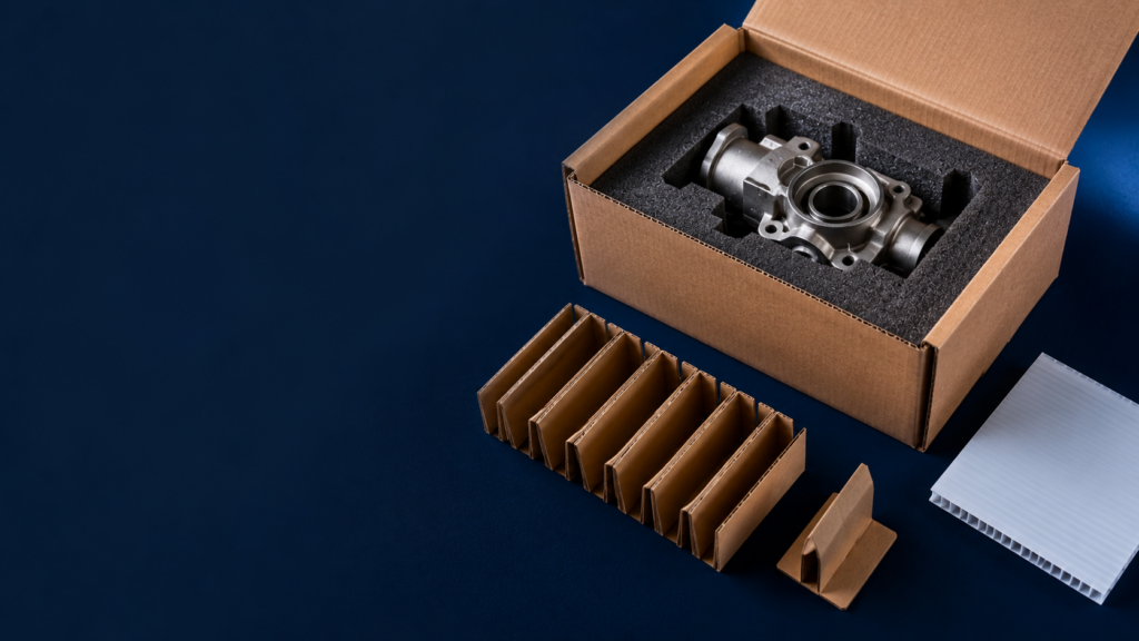 Metal mechanical component nestled in foam padding inside an open cardboard box, with protective packing separators nearby.